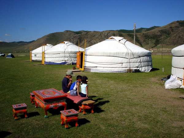photo of Mongolia, Mongolian kids sitting on traditional orange yurt furniture in a tent camp of nomads