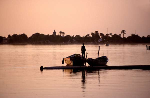 photo of Senegal, Senegalese man with two pirogues on a pier at sunset