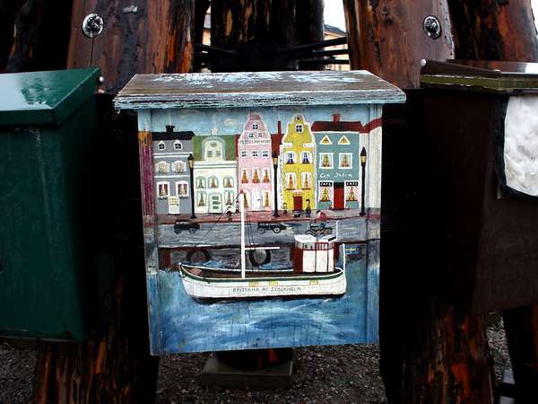 photo of Sweden, Stockholm, Skeppsholmen, nicely painted postbox with houses of Gamla Stan and a boat