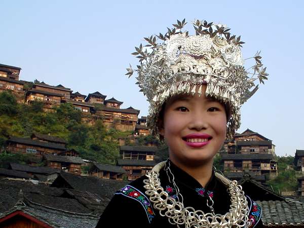 photo of China, Guizhou province, Miao girl of folklore group in traditional ethnic Miao costume, behind her the Miao village of Xining