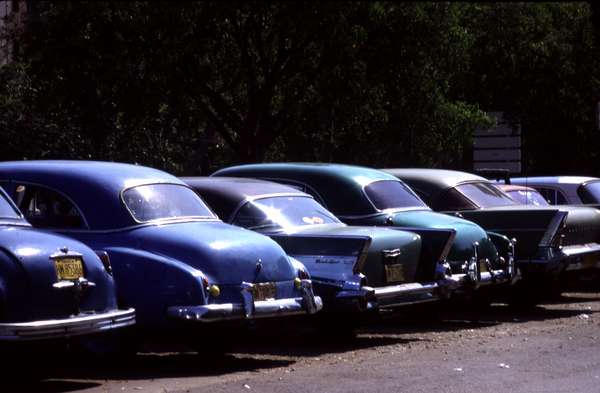 photo of Cuba, beautiful American oldtimers from the late fifties parked in the centre of Havana as in their glory days. On the inside a lot has changed : wooden structures are supporting the seats and tiny Lada engines are powering them.