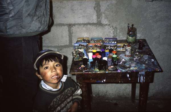 photo of Ecuador, village of Quilotoa, little Ecuadorian boy next to the working table of his father who makes Andes paintings