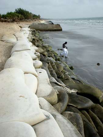 photo of The Gambia, Atlantic coast resorts, Kololi and Kotu, a Gambian man, sandbags (sand bags) on the beach of the luxurious Senegambia and Kairaba hotels.  The continued excavation of sand for construction has led to serious problems with coastal erosion