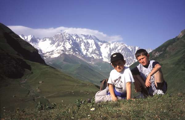 photo of Republic of Georgia, Svaneti, two Svan children in the hills around Ushguli with the white peaks op the Caucasian mount Skhara (5068 m) on the background
