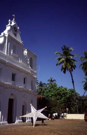 photo of India, Goa, hanging up the Christmas star on a white church among the palm trees