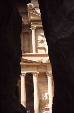 photo of Jordan, Petra temple ruins, view from between the high rock walls of the Siq (gorge) that leads into Petra, with a glimpse of the carved, colored sandstone of El Khazneh (the Treasury)