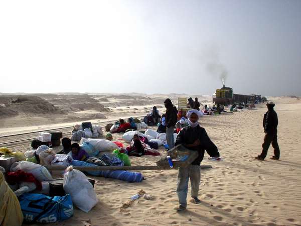 photo of Mauritania, train station of Nouadhibou, train passing through the stand outside the railway station and people waiting in the sand for the iron ore and passenger wagons