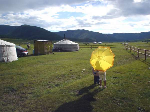 photo of Mongolia; around Terelj, hilly Mongolian landscape with two children, a yellow umbrella and a yurt (Mongolian nomads tent, yurta, ger) camp