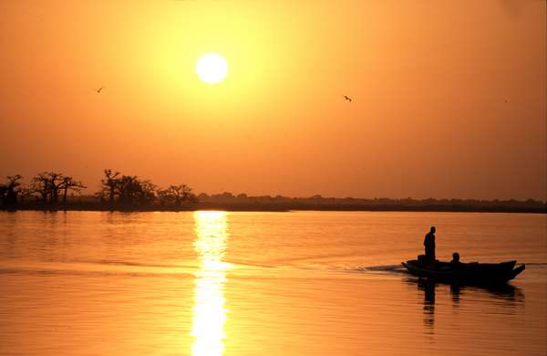 photo of Senegal, sunset over the water and mangroves of the Sine Saloum delta with fisherman in an African pirogue canoe