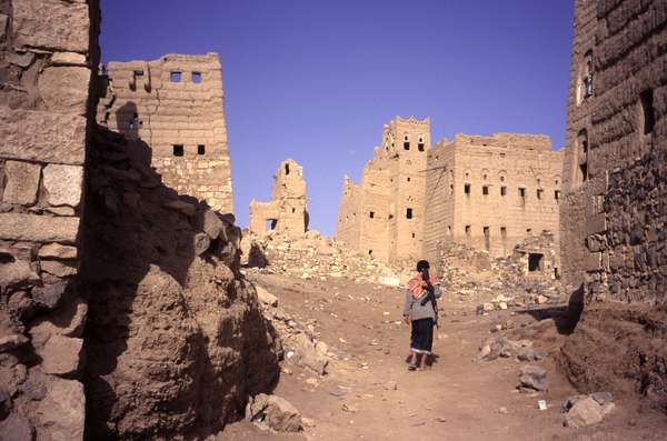 photo of Yemen, Yemeni boy with a Kalashnikov machine gun entering Marib, the ruïns of the old capital of the Kingdom of Sheba. Some of the ruins of mud brick tower houses on this archeological site have been destroyed during the civil war in the 1960's