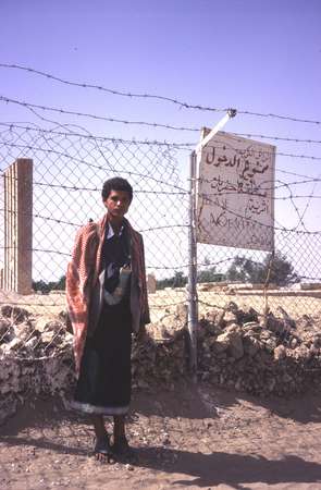 photo of Yemen, around Marib, Yemeni guard with gun and djambia dagger in front of the fence around the Sabaean Temple of the Moon