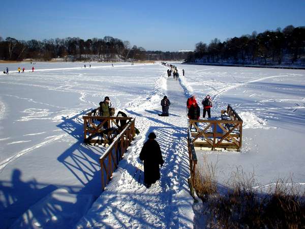 photo of Sweden, Stockholm, Haga Parken on a bright and sunny Swedish winter day : this frozen lake has been transformed in a wintersports area : people are walking and skating on the ice, skiing on the snow and ice fishing through a hole