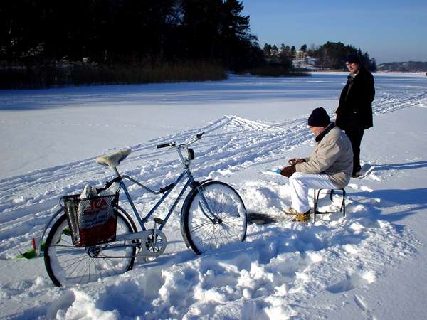 photo of Sweden, Stockholm, Haga Parken on a bright and sunny Swedish winter day : two man are ice fishing through a hole cut in this frozen lake