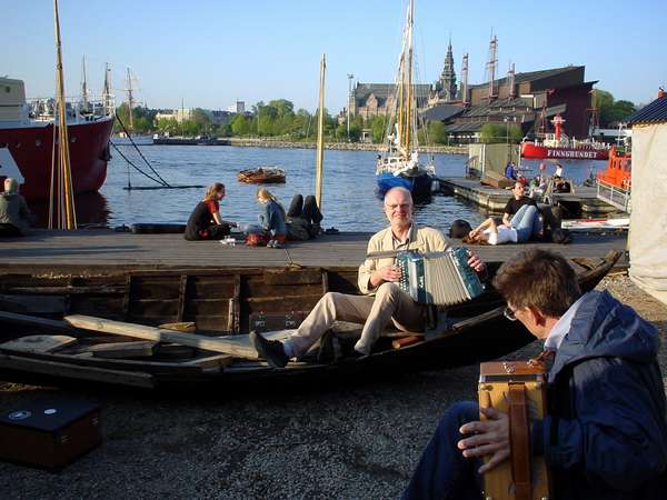 photo of Sweden, central Stockholm, Swedish folk musiscians with violin on the tiny island of Skeppsholmen in central Stockholm; on the other side of the water the Nordiska museet and Vasamuseet
